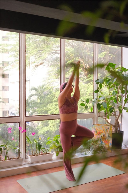 Person practicing yoga in a room with large windows and greenery
