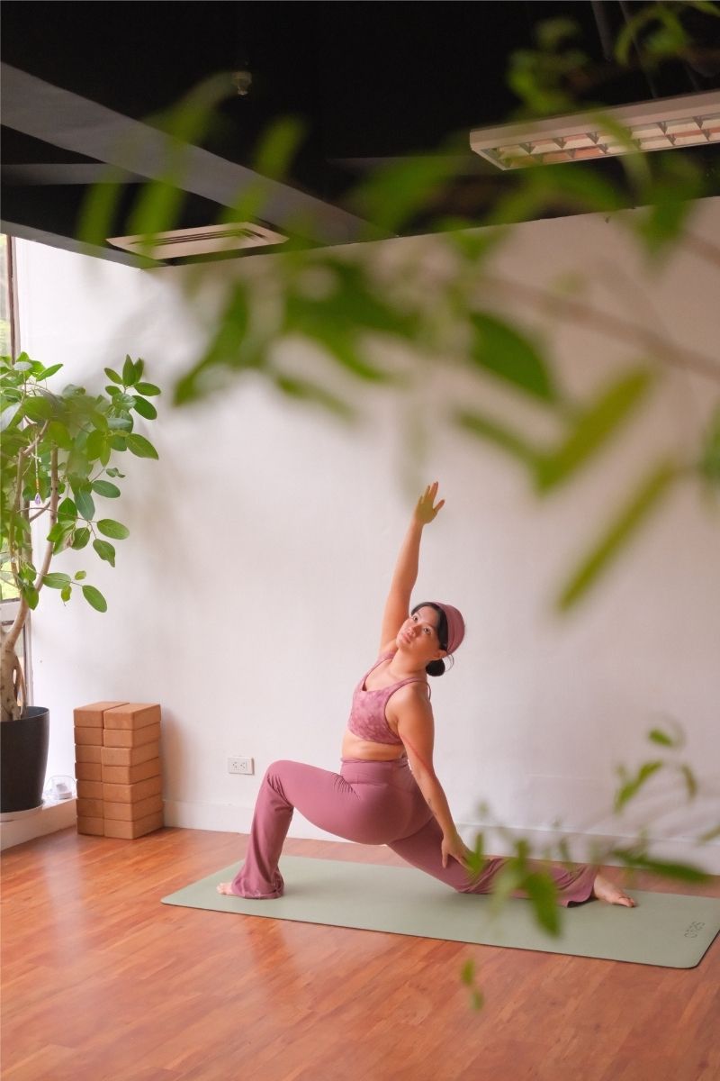 Woman practicing yoga in a room with plants and wooden floor